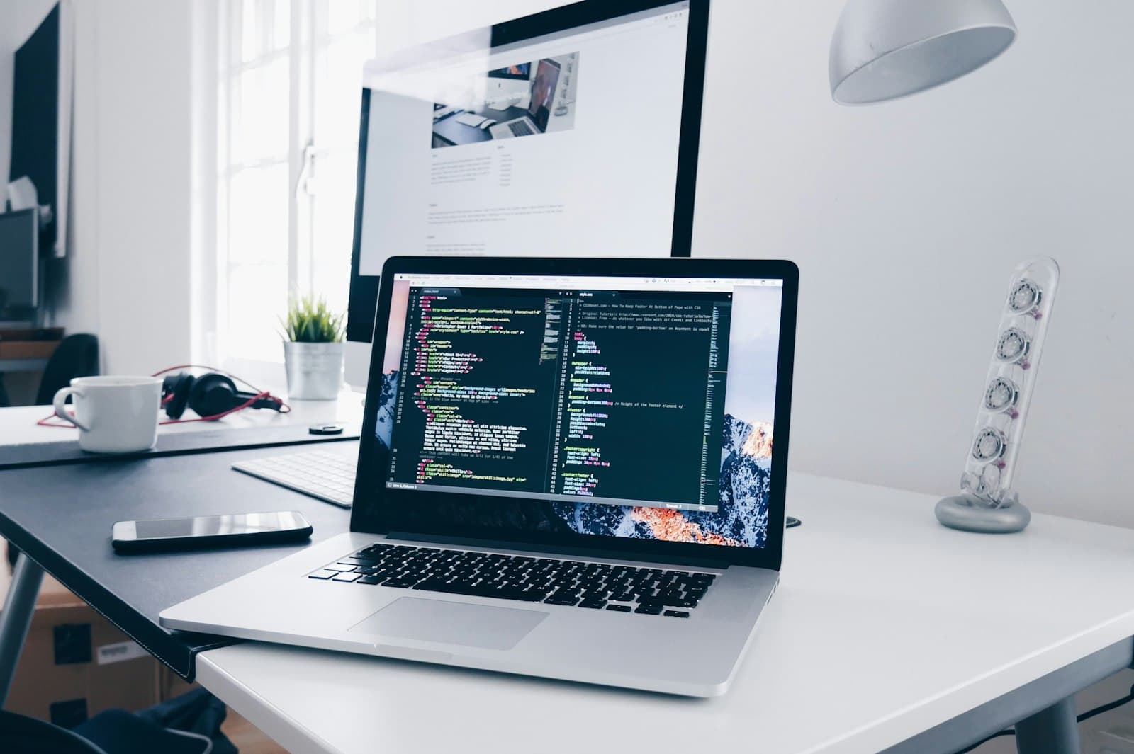 MacBook mit geöffnetem Code-Editor auf einem aufgeräumten Schreibtisch
